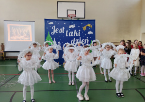 Uczennice klas młodszych w białych strojach prezentują taniec z wiankami podczas koncertu świątecznego.
