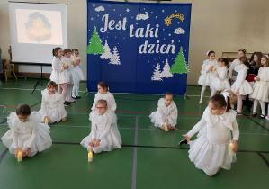 Uczennice w białych strojach wykonują taniec ze świecami podczas koncertu świątecznego na sali gimnastycznej.