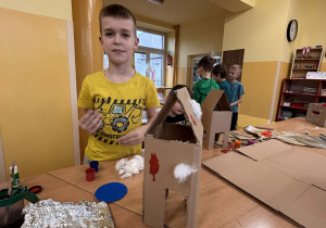Uczeń w świetlicy szkolnej prezentuje kartonowy karmnik dla ptaków wykonany podczas zajęć.