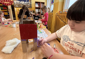 Uczeń w świetlicy szkolnej maluje kartonowy karmnik dla ptaków podczas zajęć plastycznych.