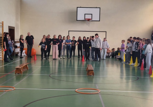 Uczniowie i nauczyciele stoją przy torze sprawnościowym w sali gimnastycznej.