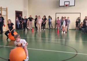 Uczniowie i nauczyciele pokonują tor na piłkach do skakania w sali gimnastycznej.