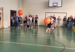 Uczniowie i nauczyciele rywalizują z piłkami do skakania w sali gimnastycznej.